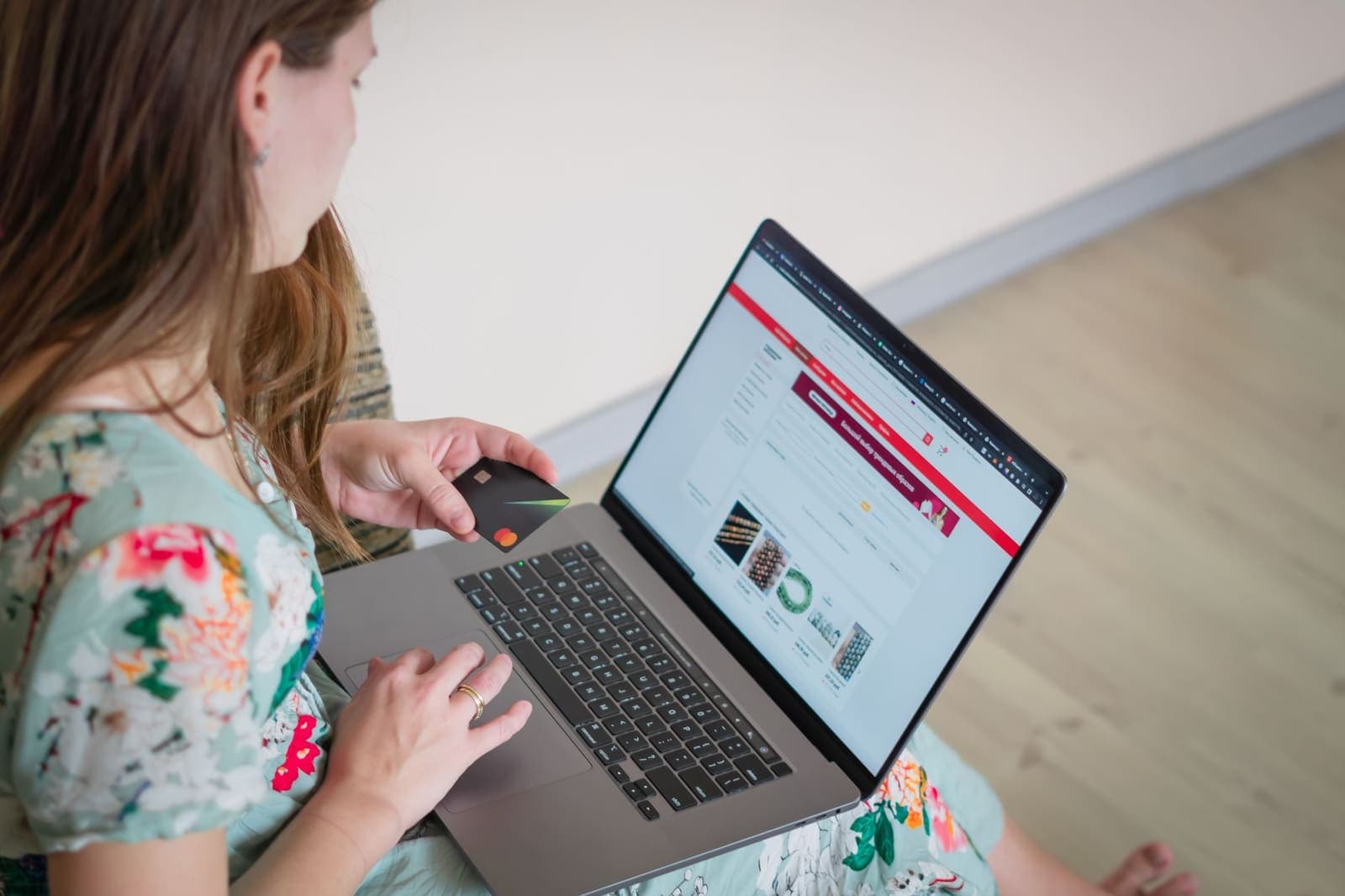 Frau kauft online am Laptop ein und hält dabei eine Bankkarte in der Hand