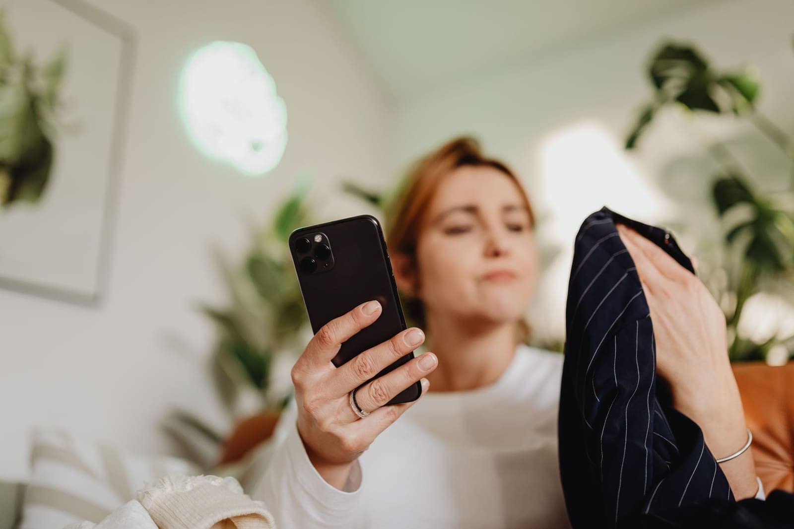 Frau betrachtet ein Kleidungsstück und sucht auf ihrem Handy nach einem Rabattcode